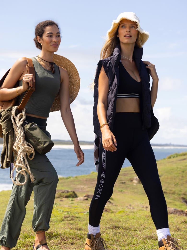 Two women walking on grass with water in the background